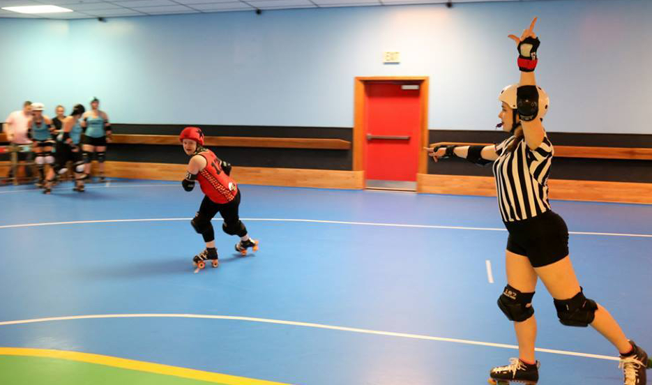 A roller derby skater strides, a ref points at her