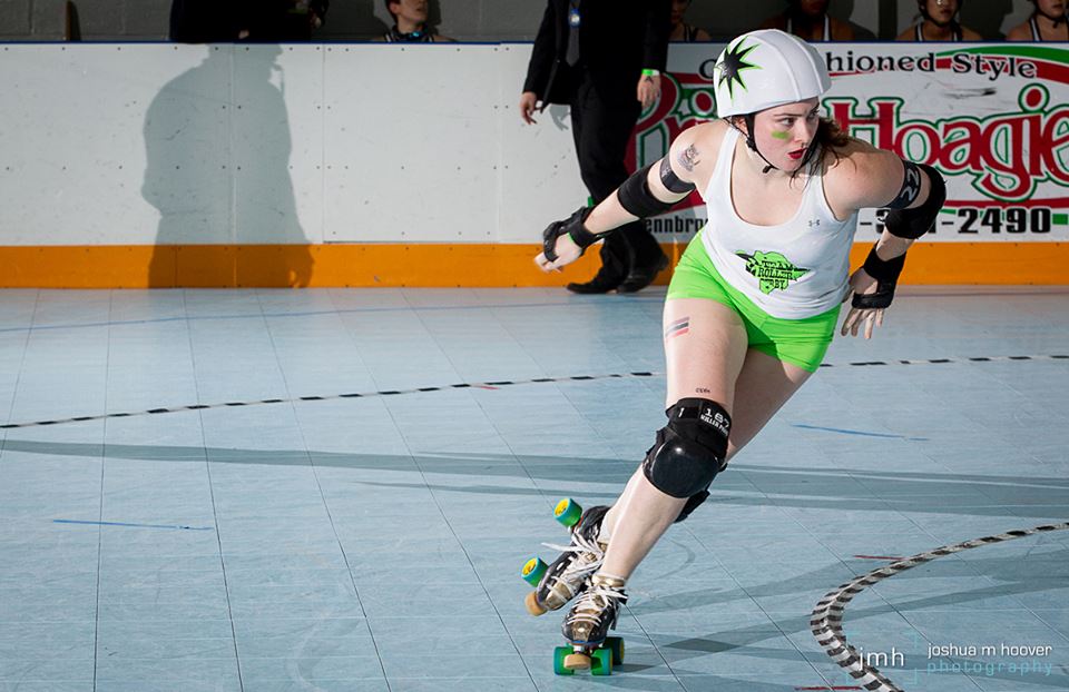 A jammer skates around the roller derby track in green shorts